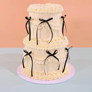 2 Tier Vintage Cake with cream frosting, black ribbon decorations, perfect for weddings by Crumbs & Doilies.